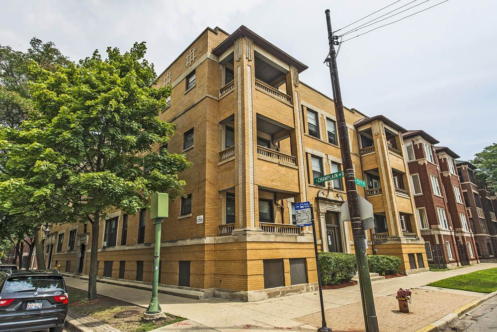 A yellow brick apartment building with balconies, trees, and a street sign.