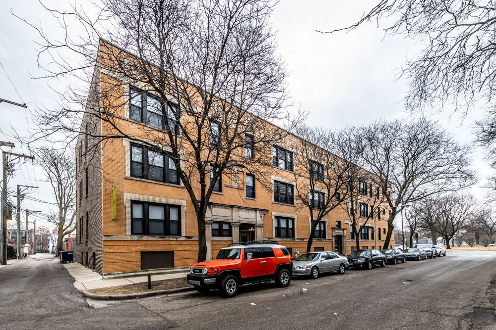 Orange Jeep parked in front of a brick apartment building with cars parked alongside.
