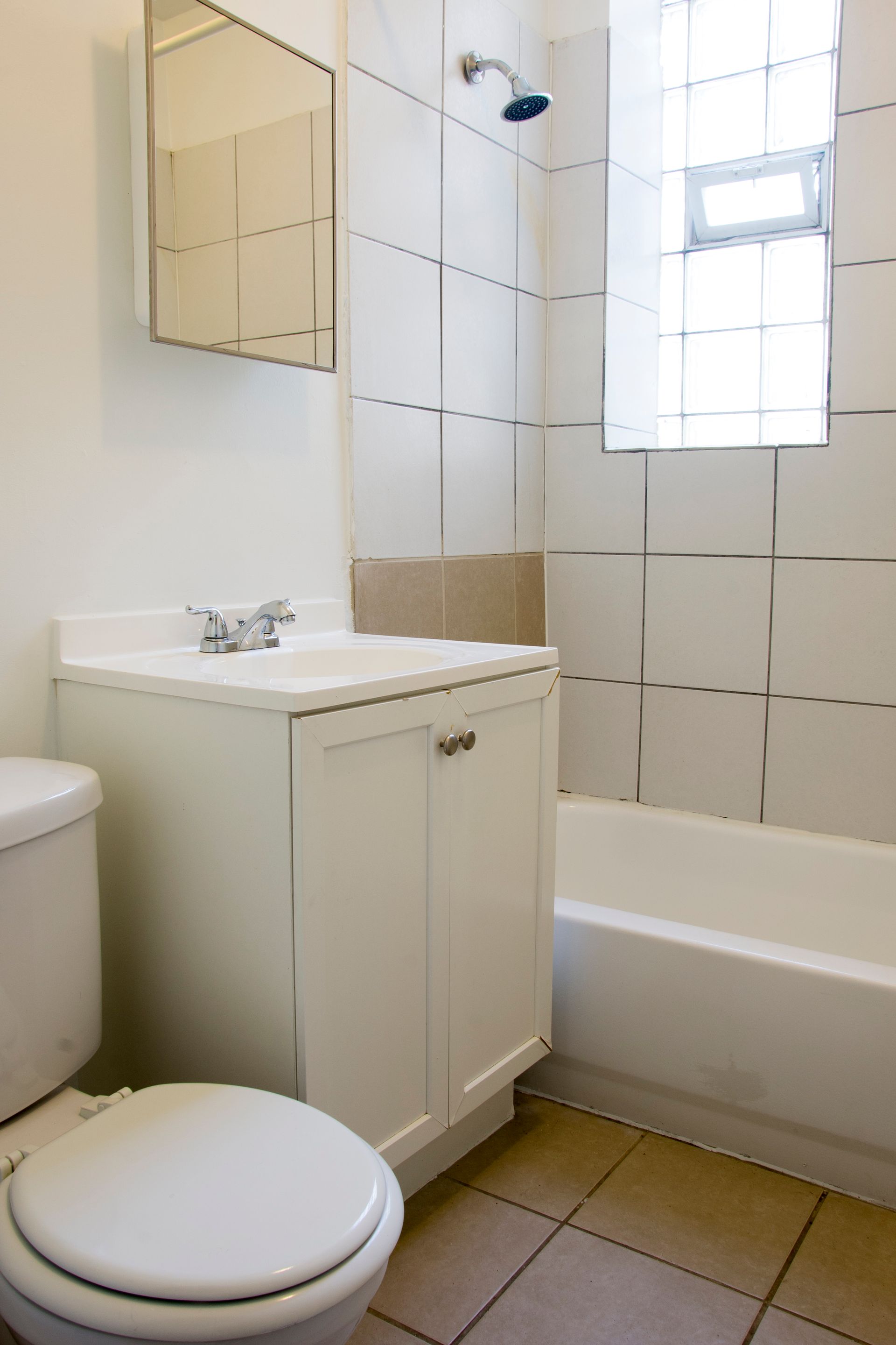 Bathroom with a white toilet, sink, and tub, tiled walls, and a window.