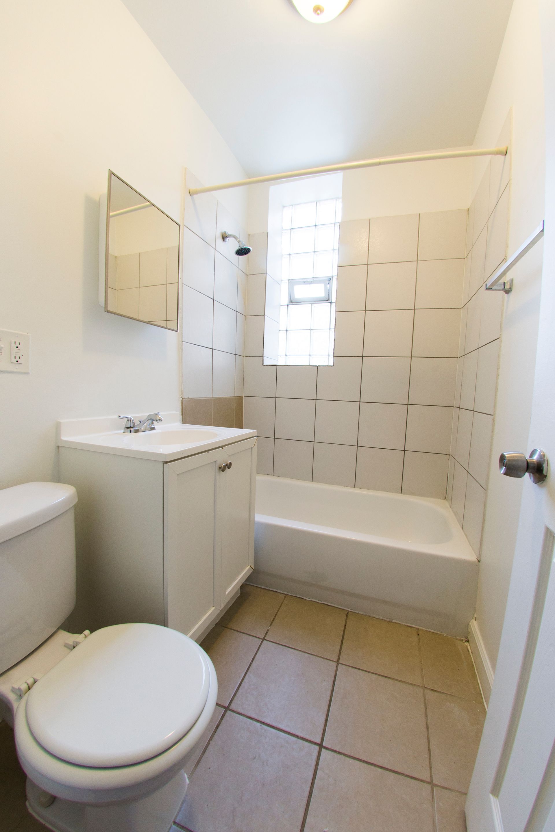 Bathroom with a white vanity, toilet, and bathtub. Beige tiled floor.