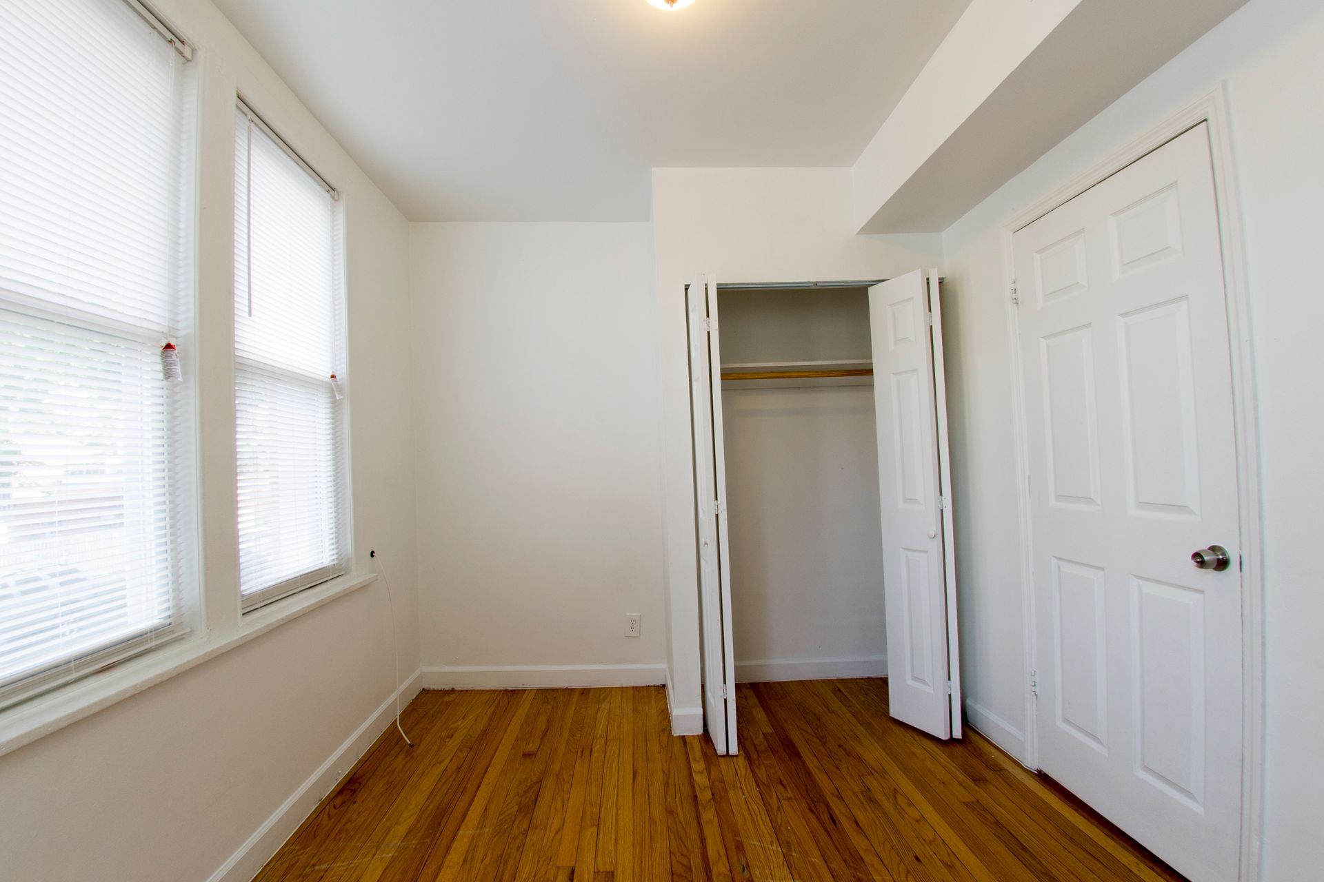 Empty room with hardwood floors, white walls, closet, and two windows with blinds.