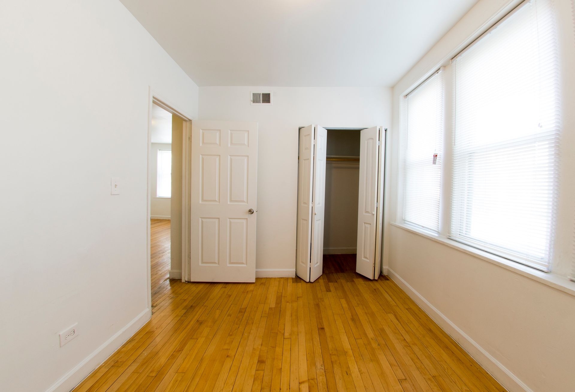 Empty room with hardwood floors, white walls, closet, door, and window with blinds.