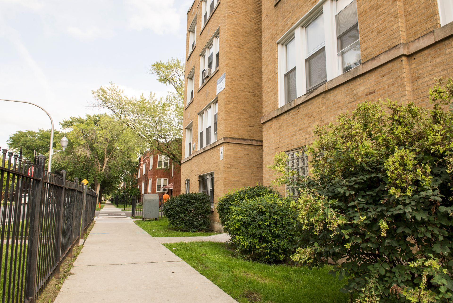 Sidewalk alongside a brick apartment building and a small red brick house.
