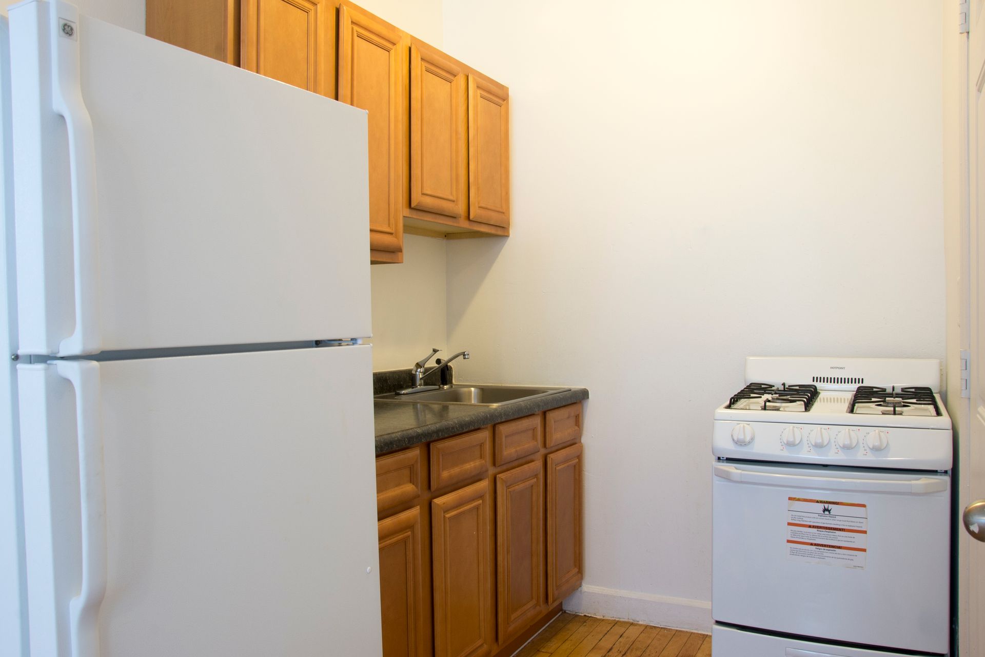 Small kitchen with white refrigerator, stove, wooden cabinets, and sink.