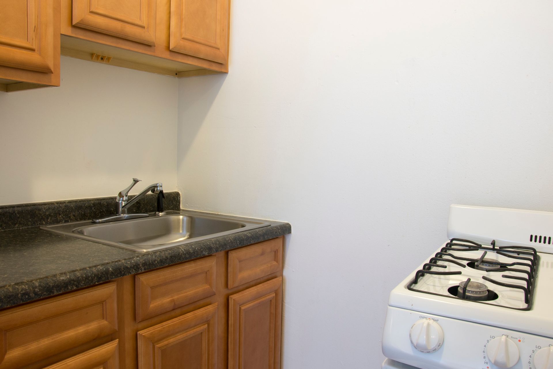 Kitchen with light brown cabinets, dark countertop, stainless steel sink, and white stove.