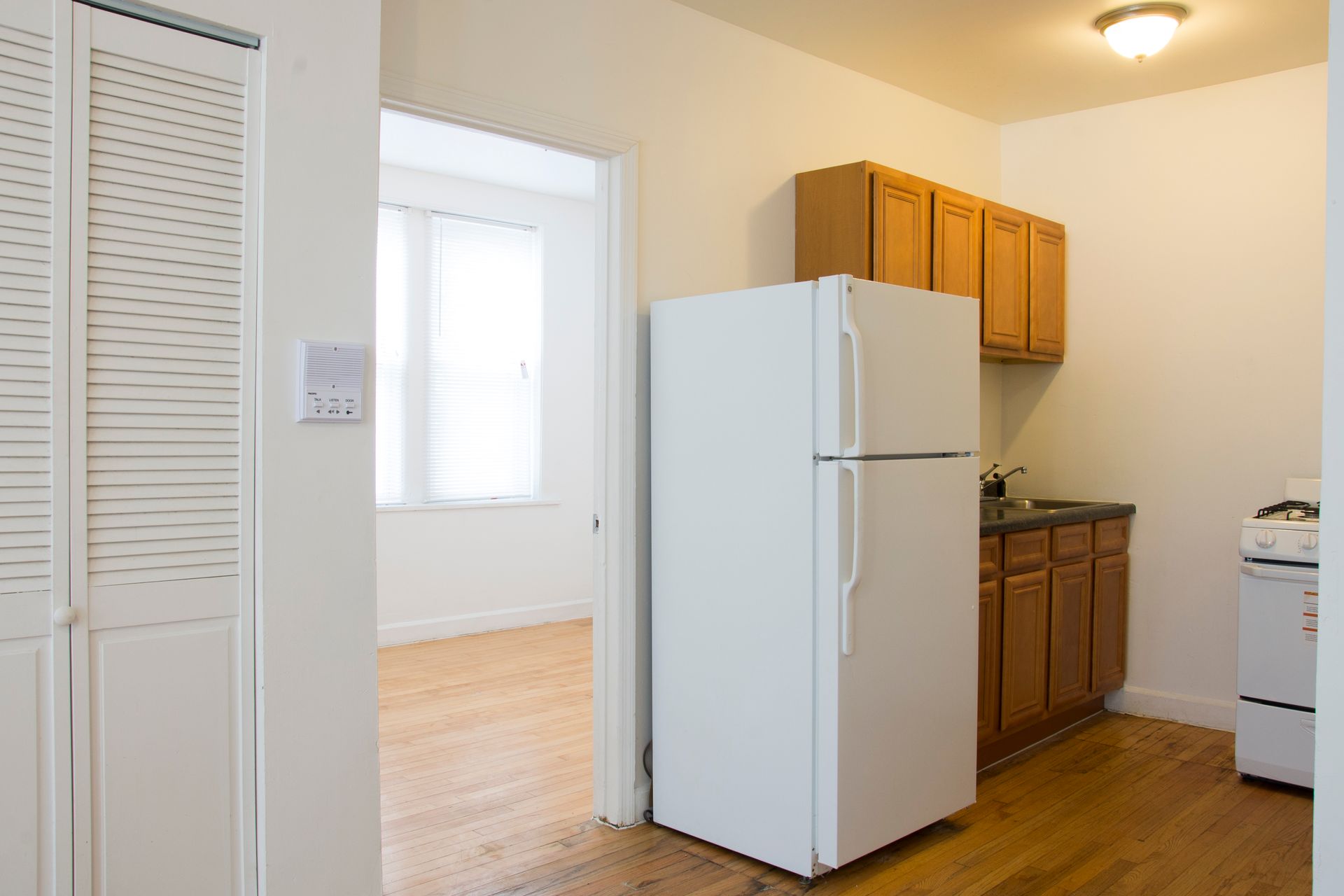 Kitchen and hallway with white refrigerator, wooden cabinets, and a doorway to another room.