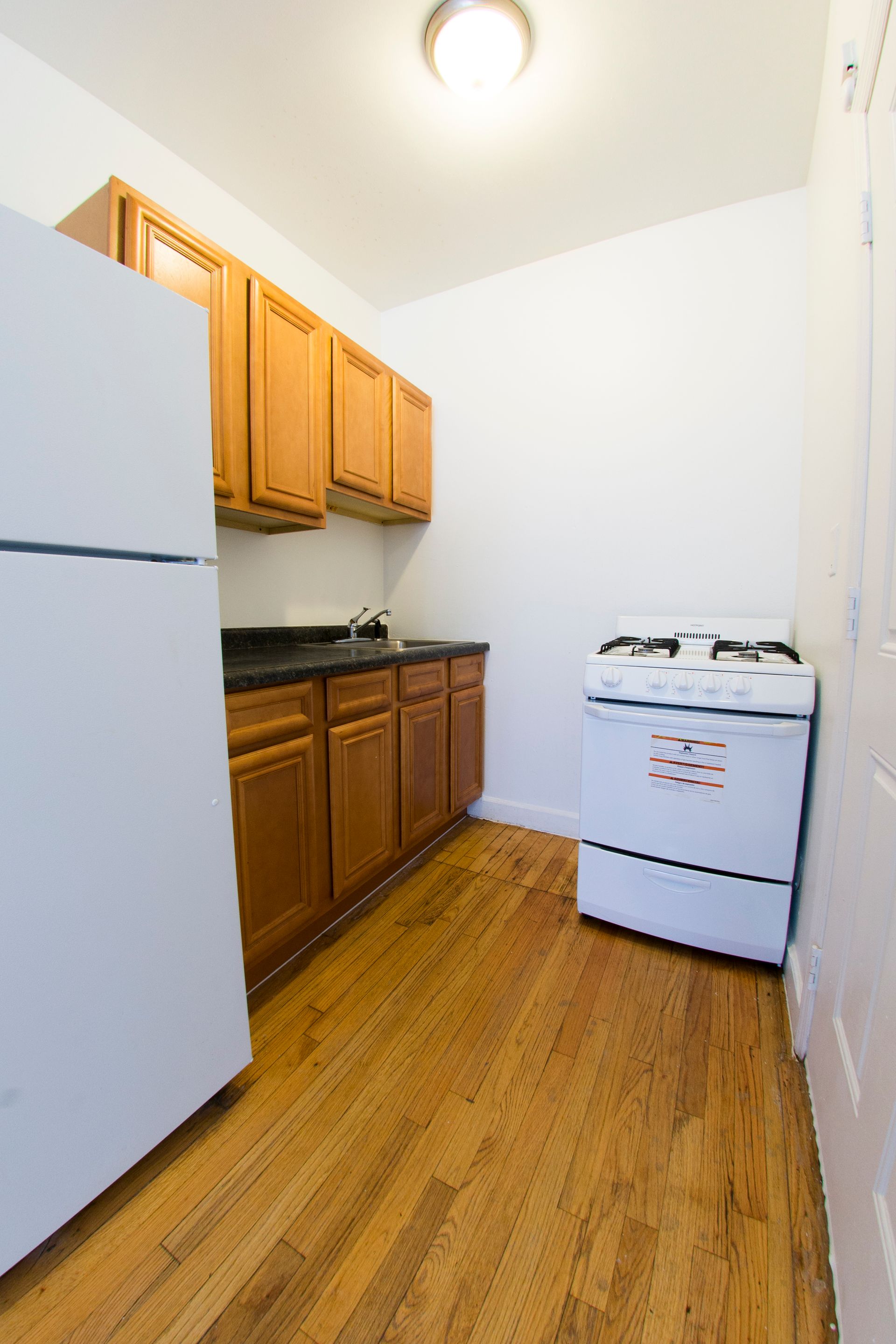 Small kitchen with white appliances, wooden cabinets and flooring.