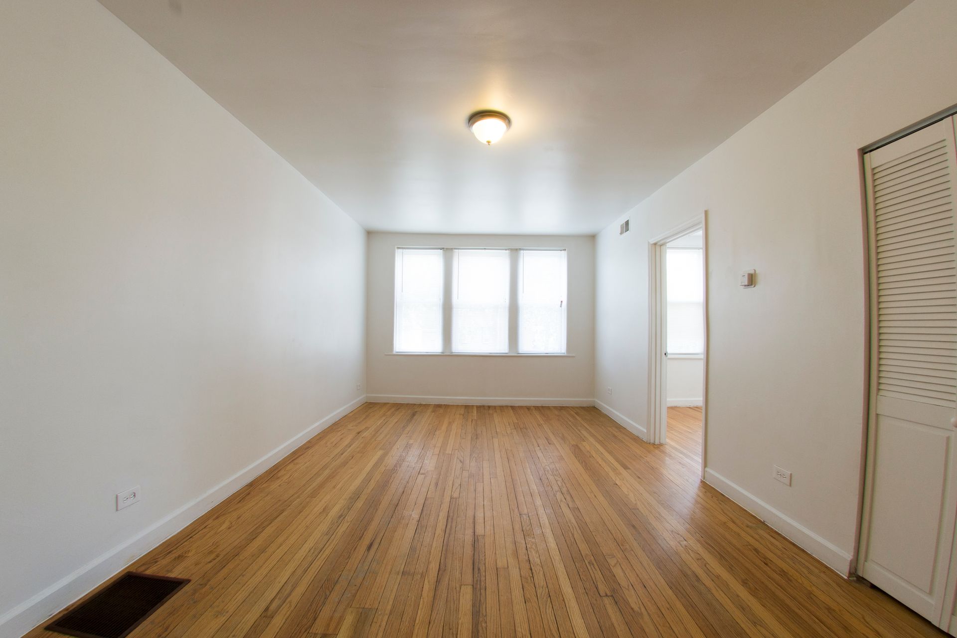 Empty room with wood floor, white walls, windows, and a doorway.