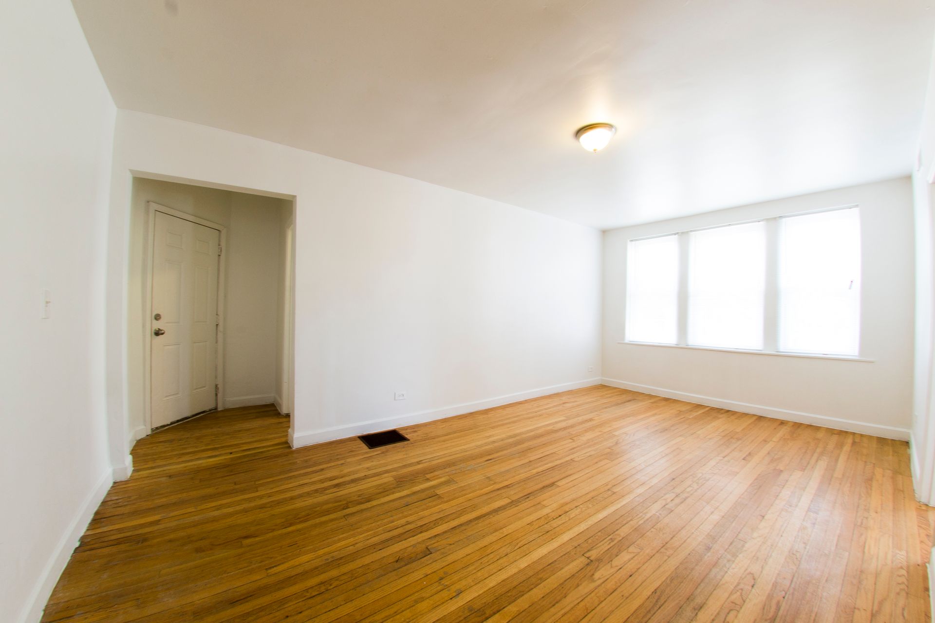 Empty room with hardwood floors, white walls, and a window.