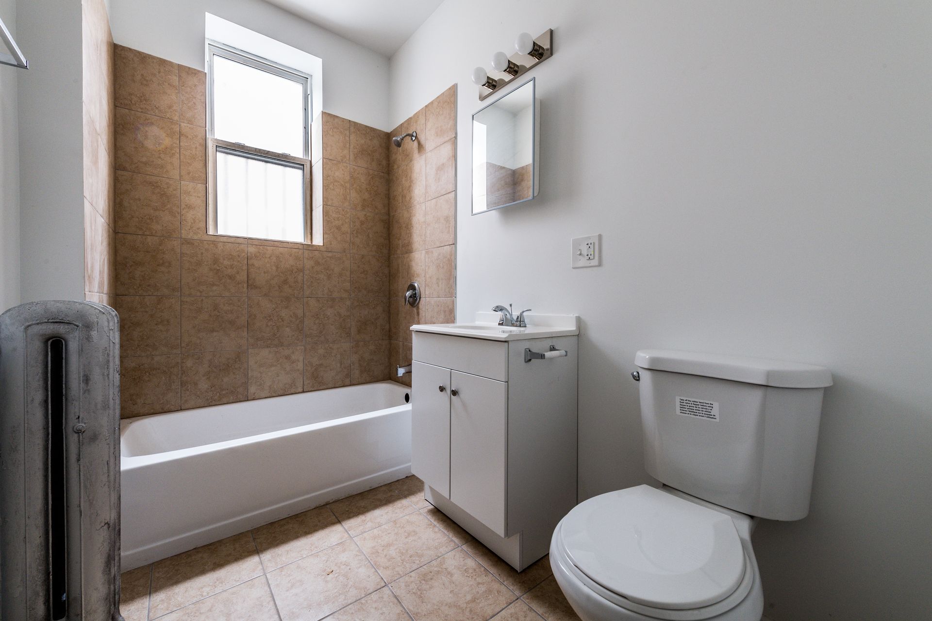 Bathroom with white toilet, vanity, and bathtub; tan tile shower surround, window.