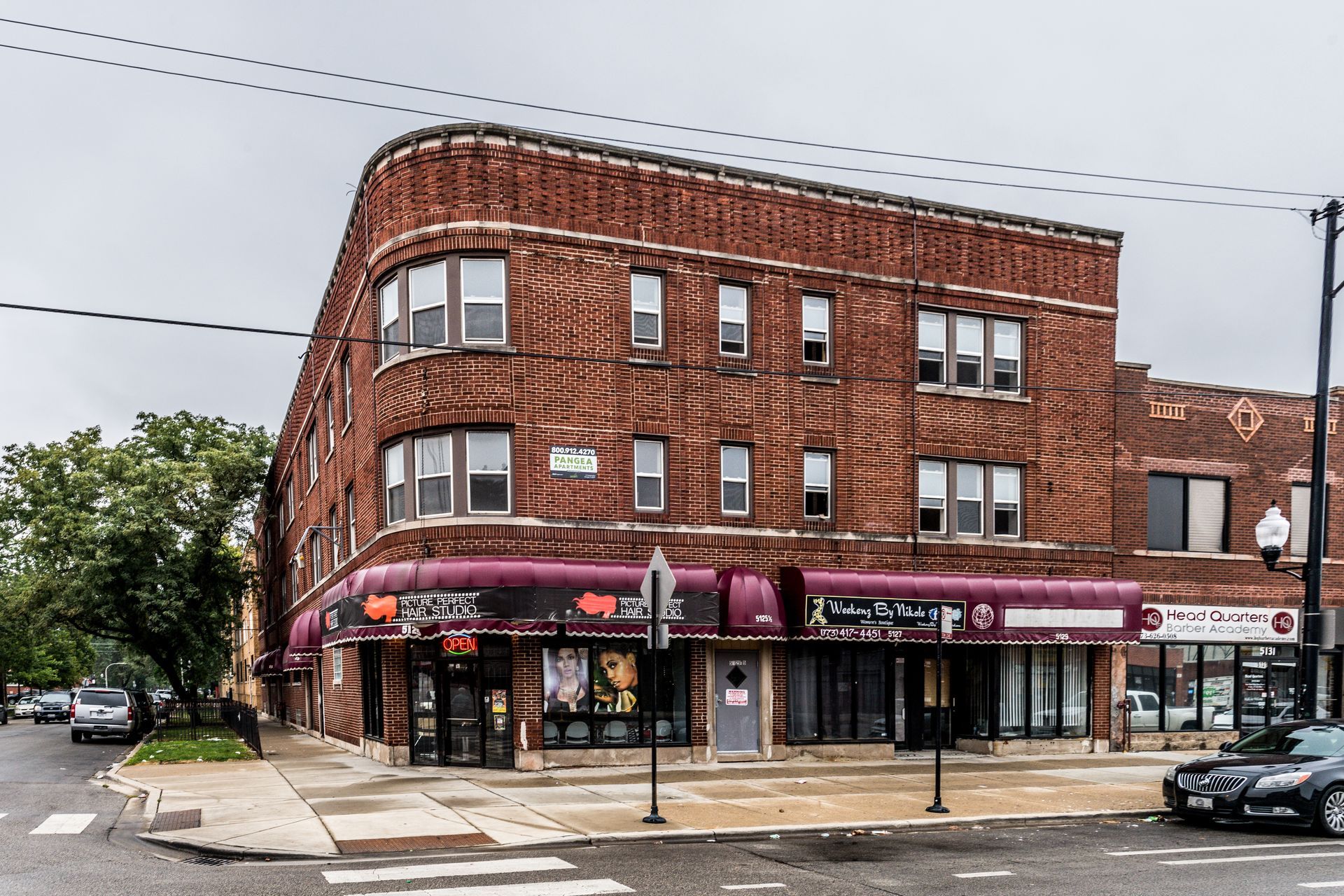 Brick building with businesses on the ground floor; corner lot, cloudy sky.