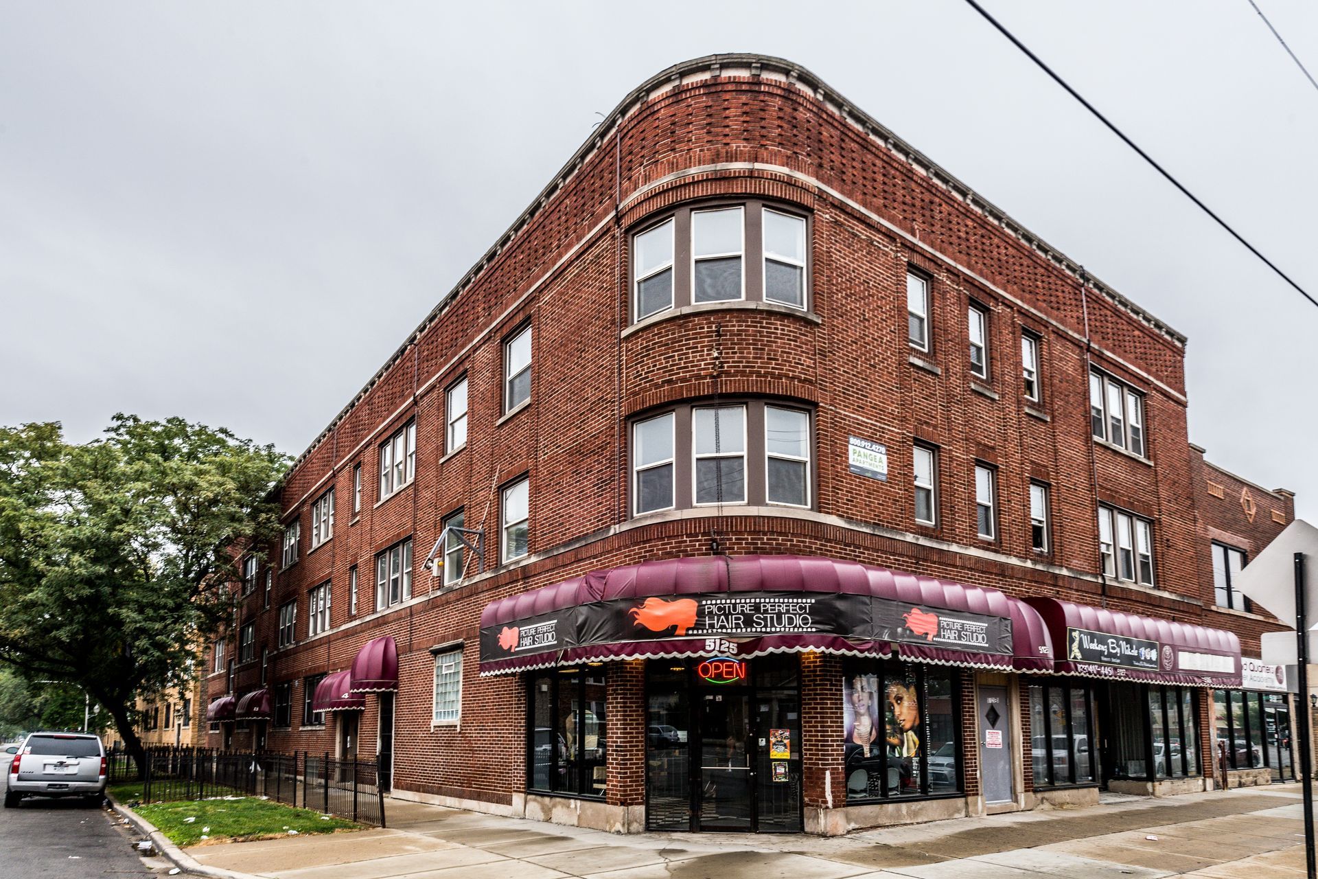 Red brick corner building with storefronts and awnings under a cloudy sky.