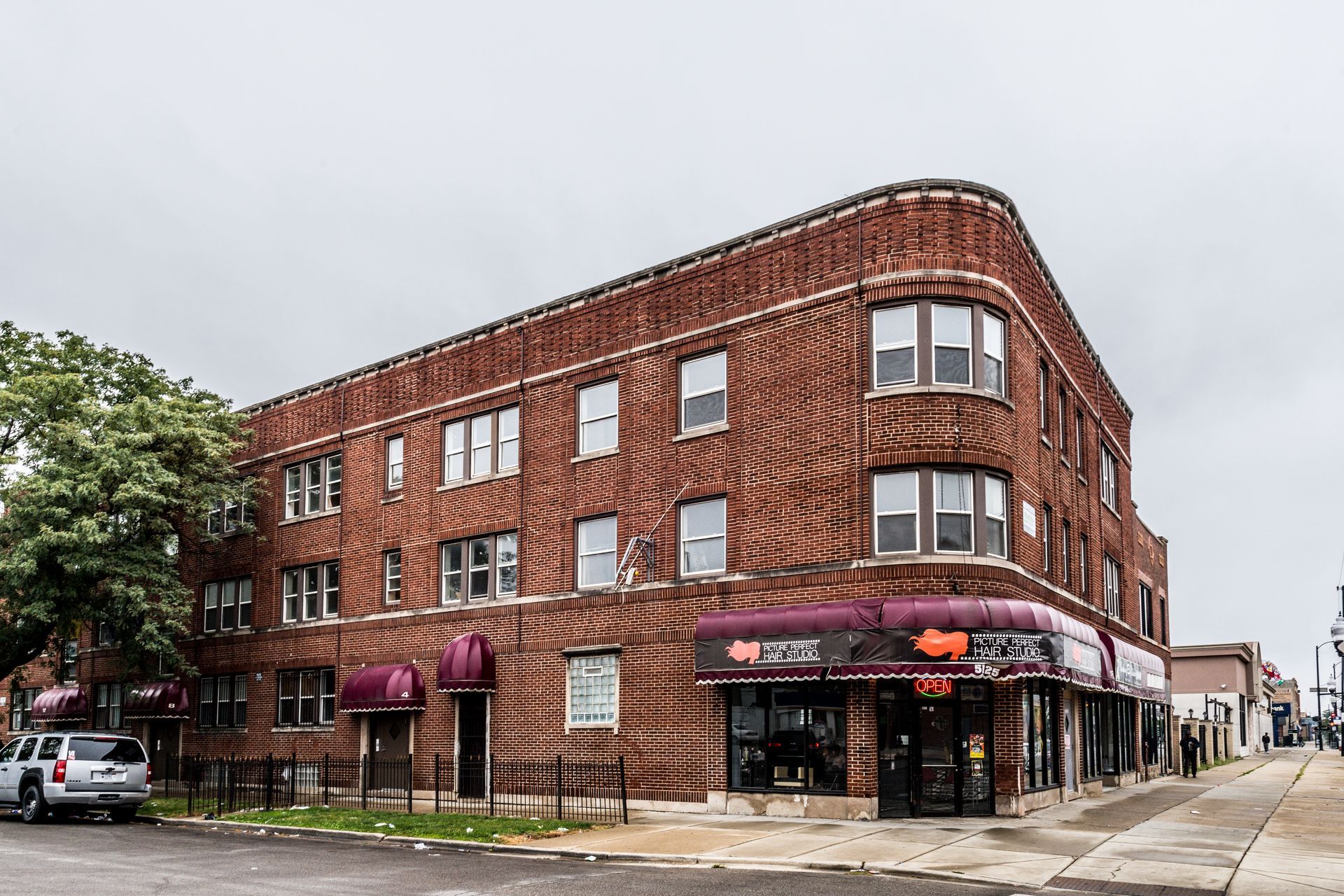Brick building with commercial storefronts and apartments, cloudy sky overhead.