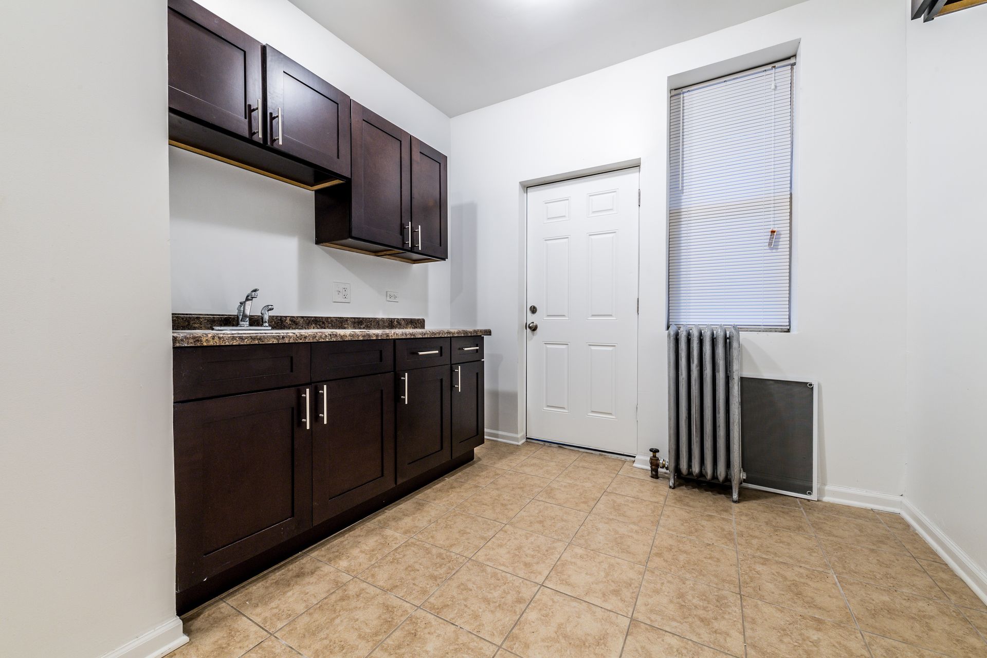Small kitchen with dark brown cabinets, granite countertops, and a white door and window.