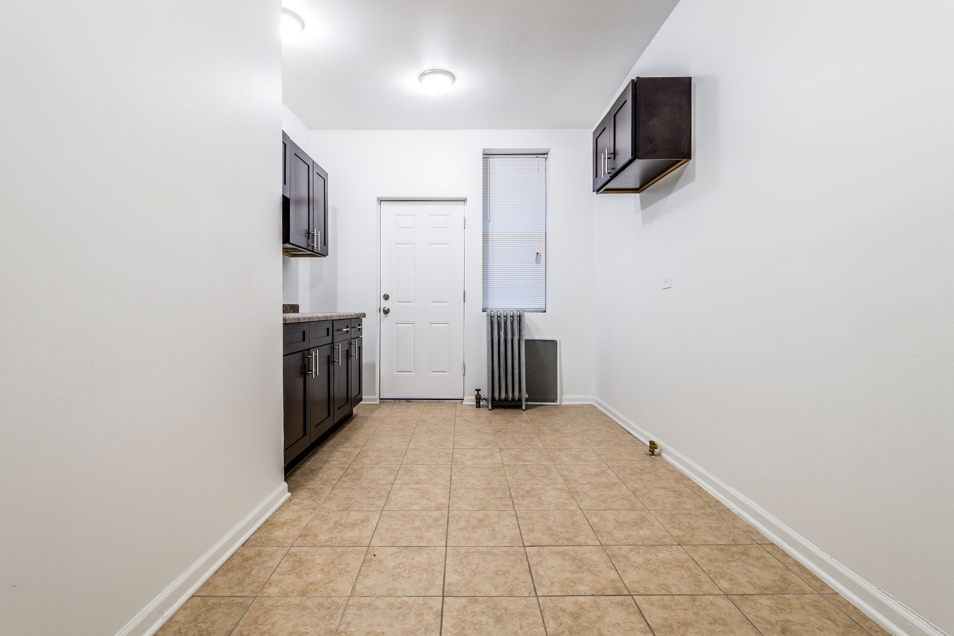 Empty kitchen with dark brown cabinets, tile floor, and a white door.