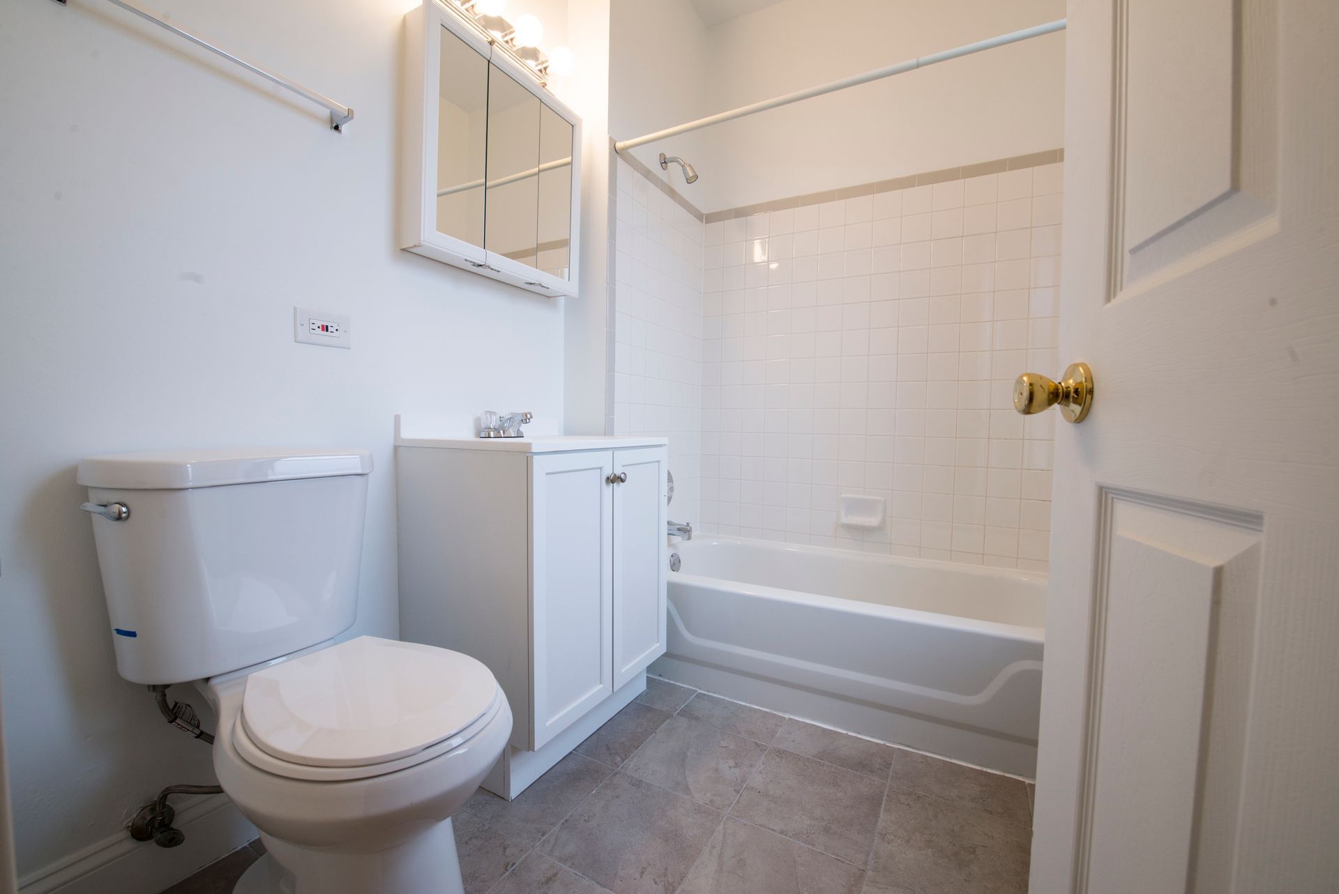 Bathroom with white toilet, vanity, and bathtub; door open to the right.
