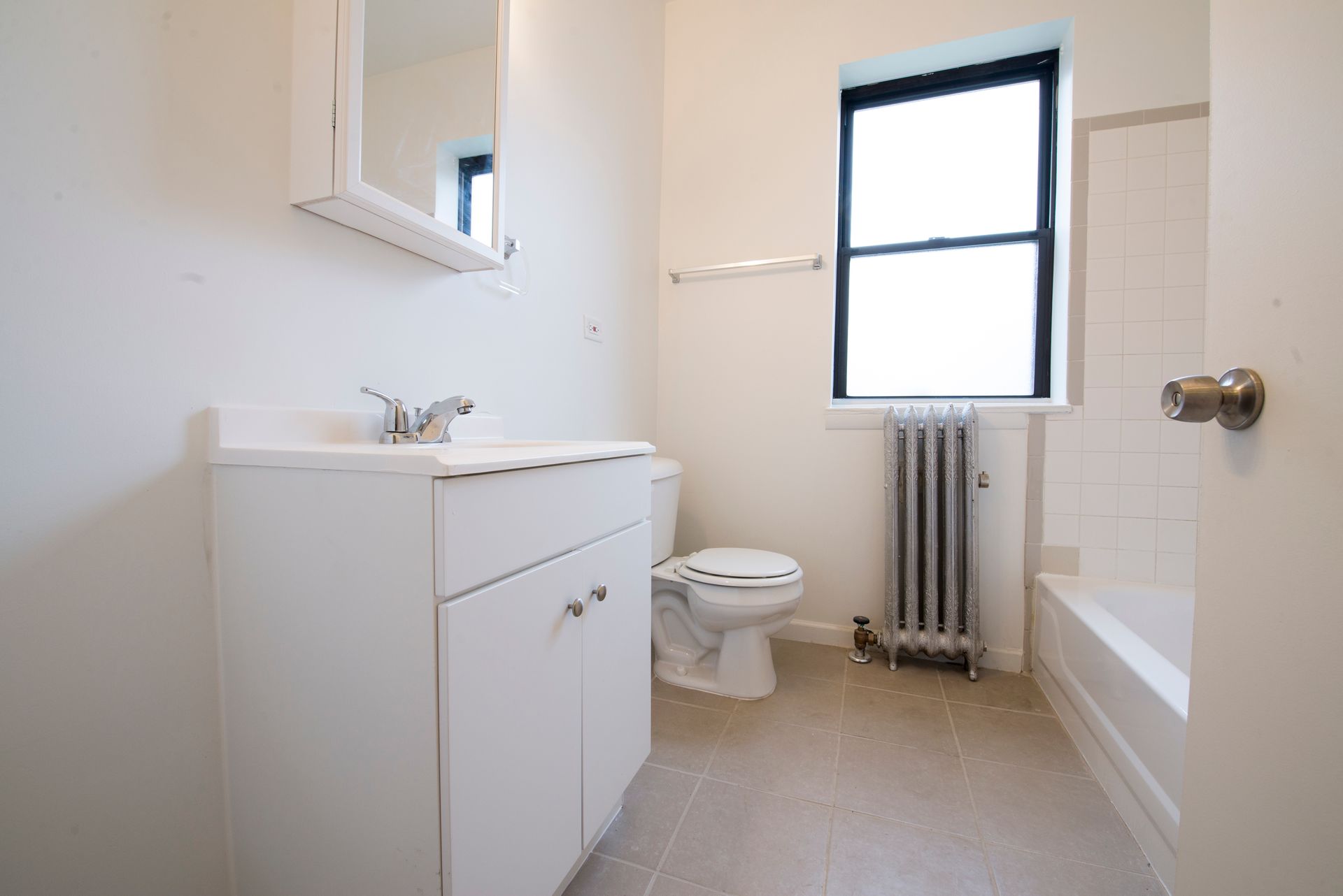 White bathroom with a vanity, toilet, window, and radiator.