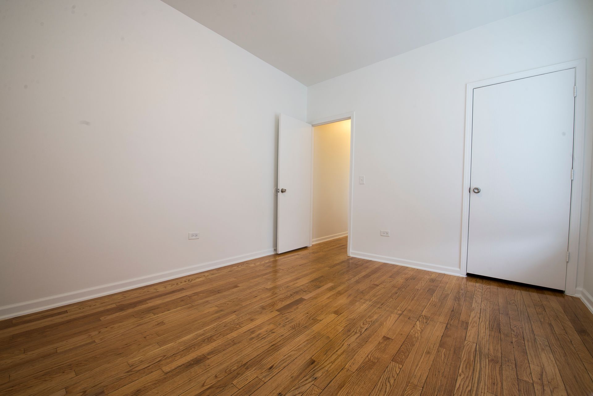 Empty room with hardwood floors, white walls, and two closed doors.