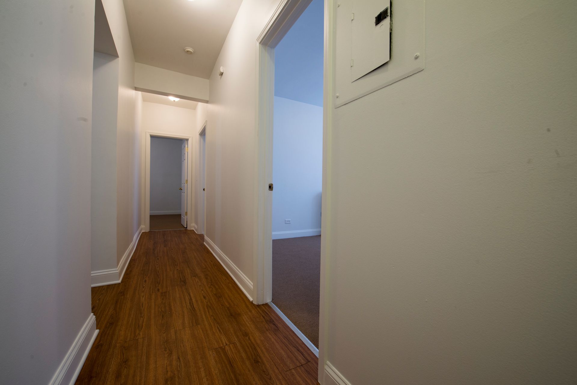 Long hallway with wood flooring, white walls, and open doorways.