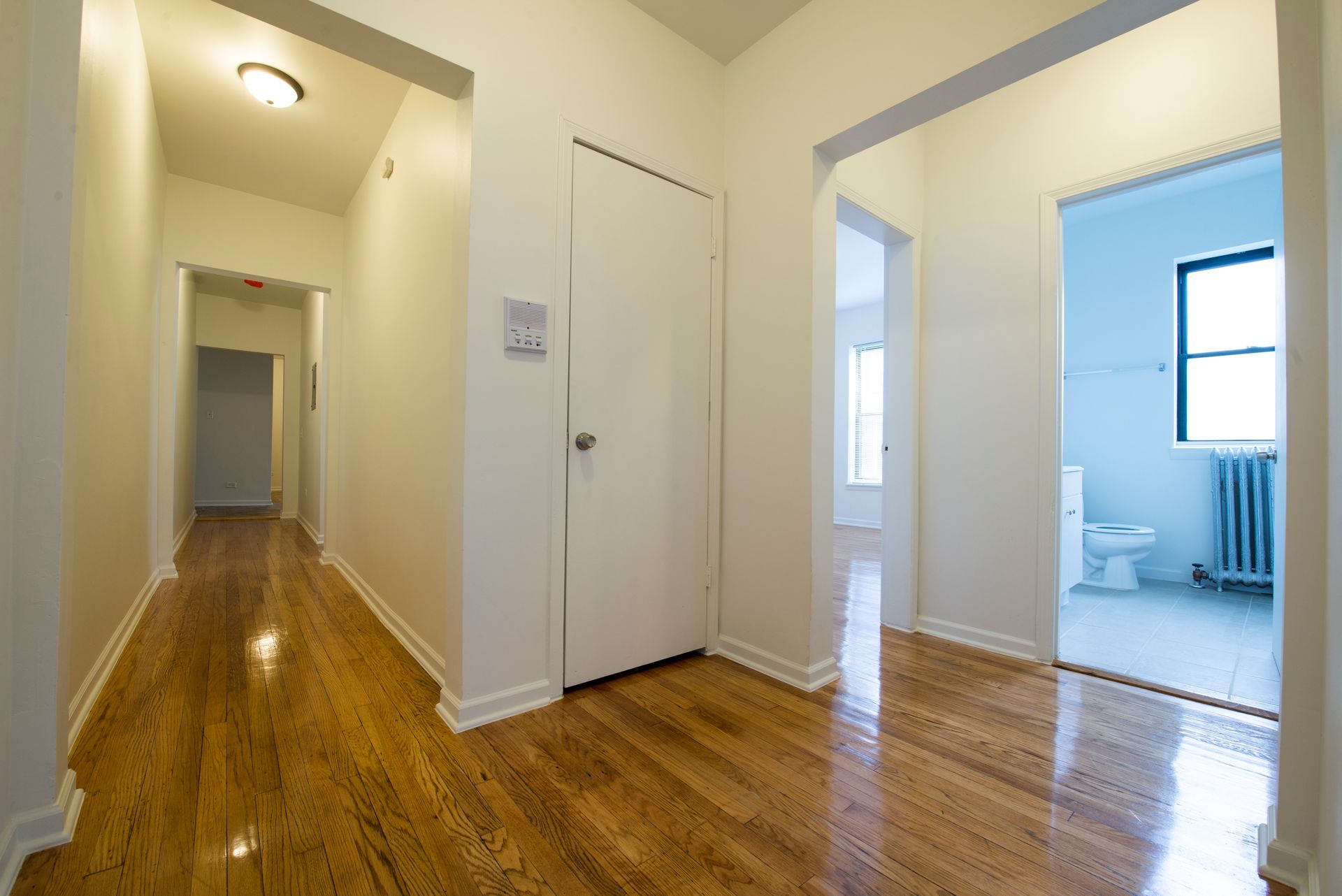 Long hallway with hardwood floors, white walls, and doorways leading to rooms.