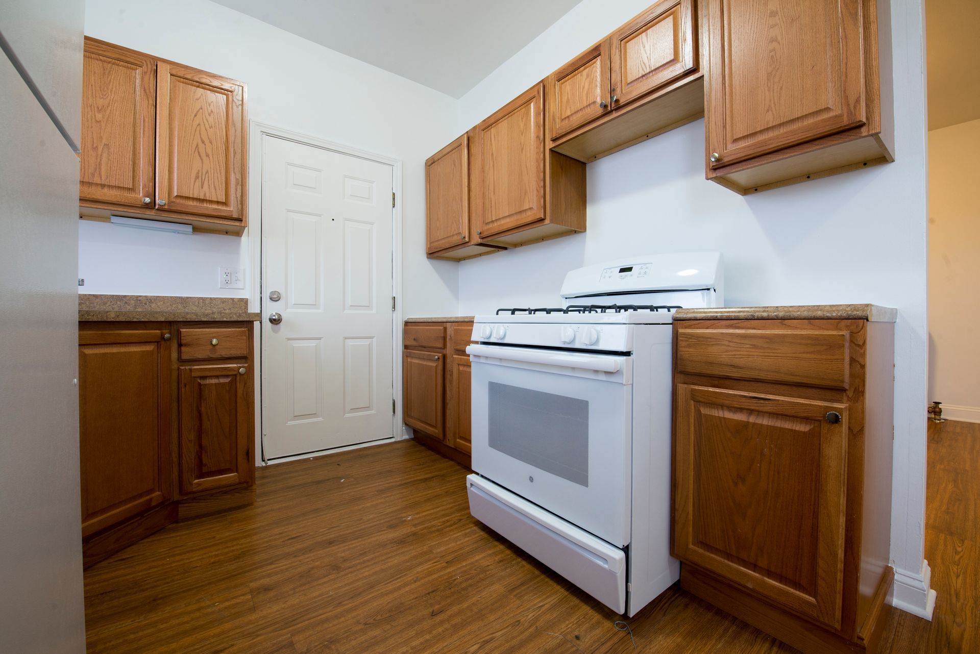Kitchen with wood cabinets, white stove, and door on a wood floor.
