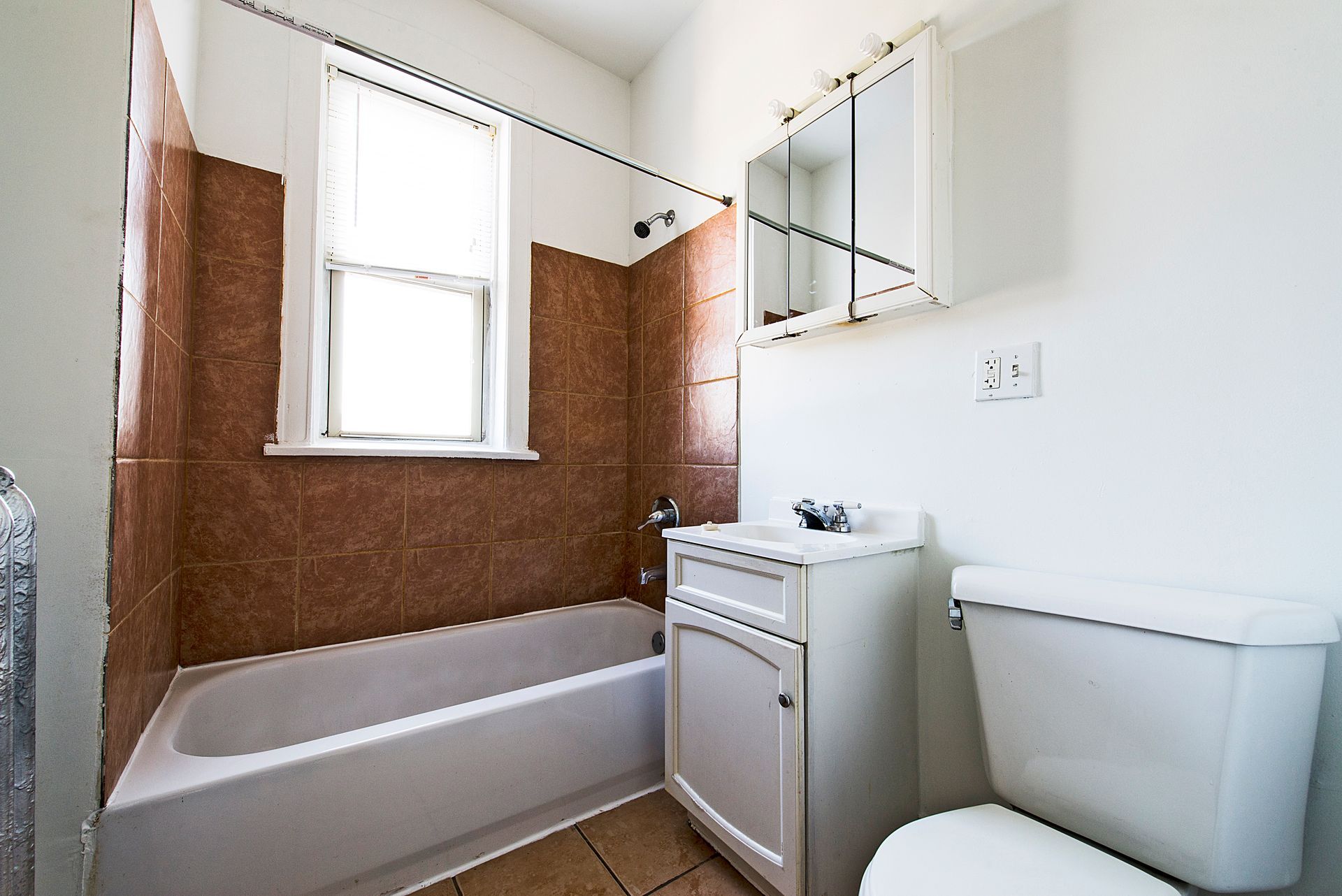 Bathroom with white toilet and sink, brown tiled wall, and window.