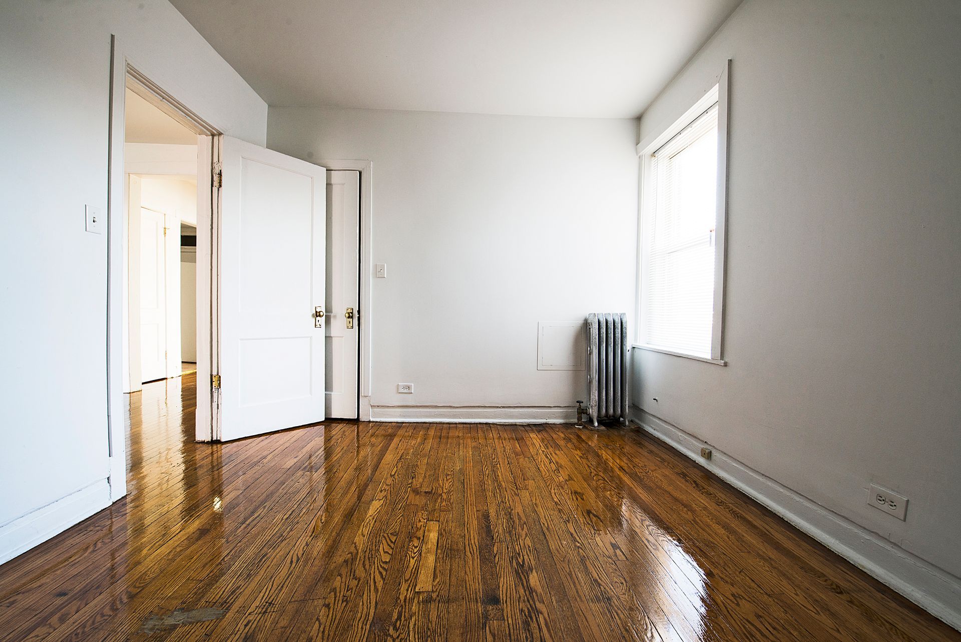 Empty room with hardwood floors, white walls, open doors, and a window.