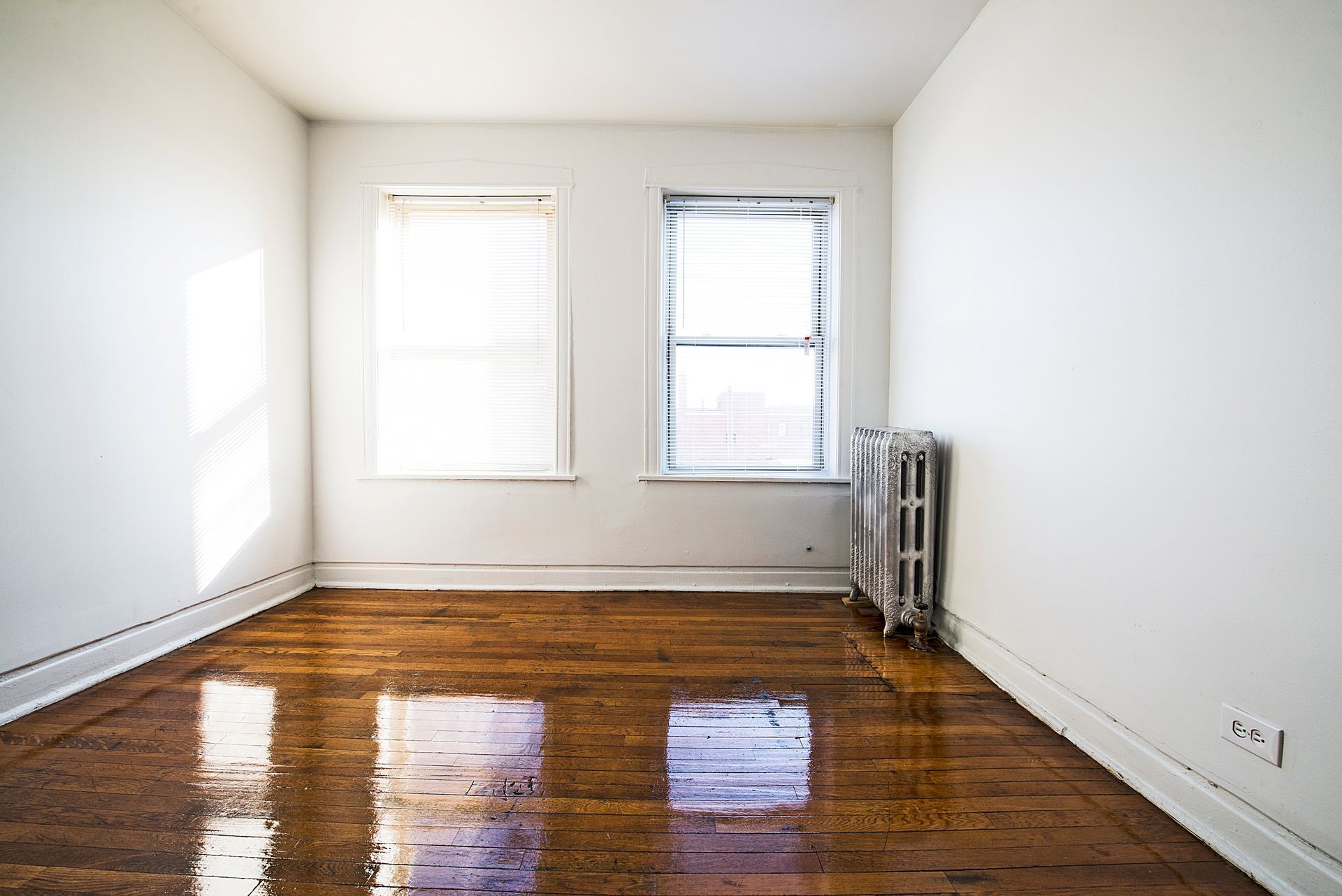 Empty room with two windows, radiator, and hardwood floor.