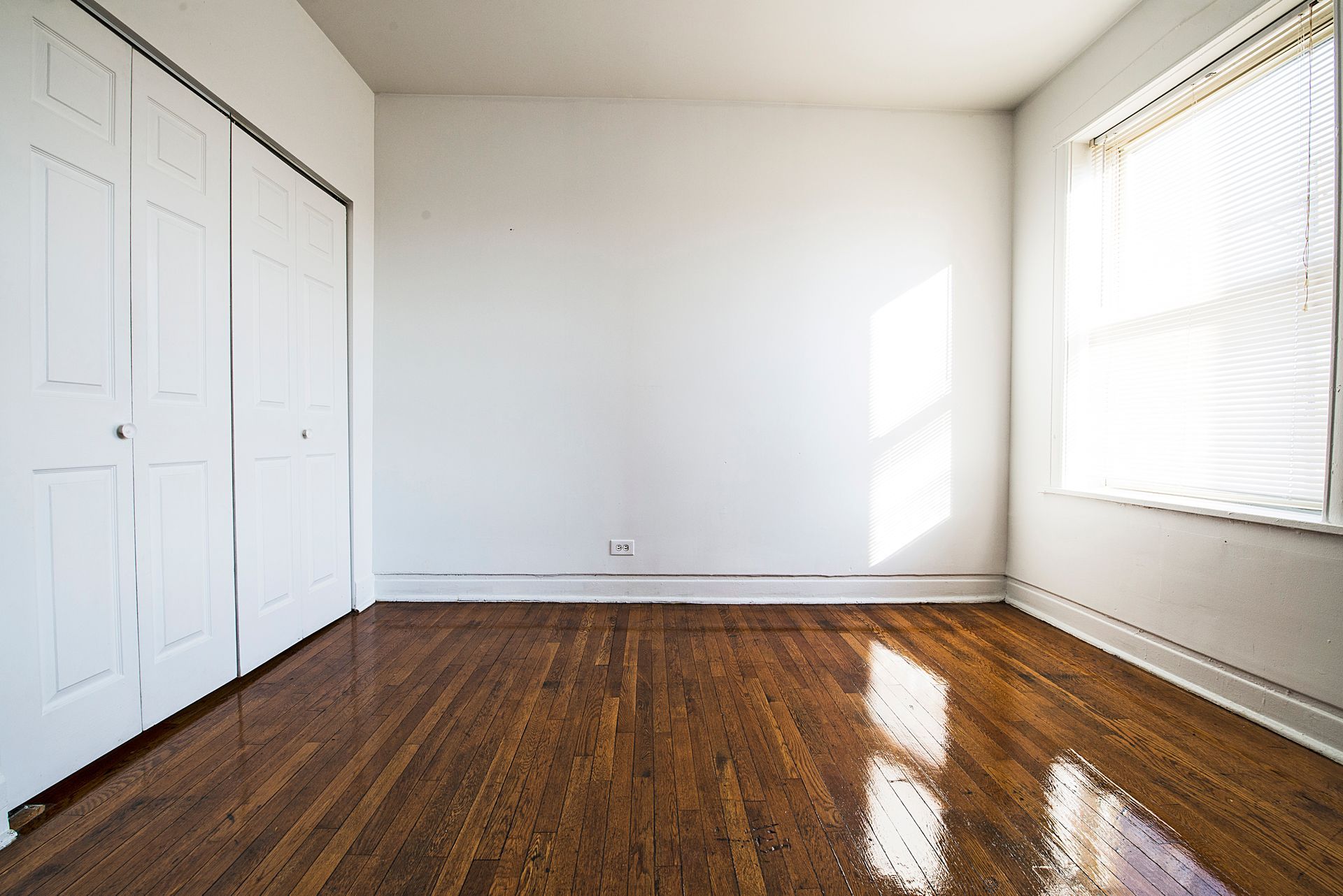Empty room with hardwood floors, white walls, closet, and a window with sunlight.