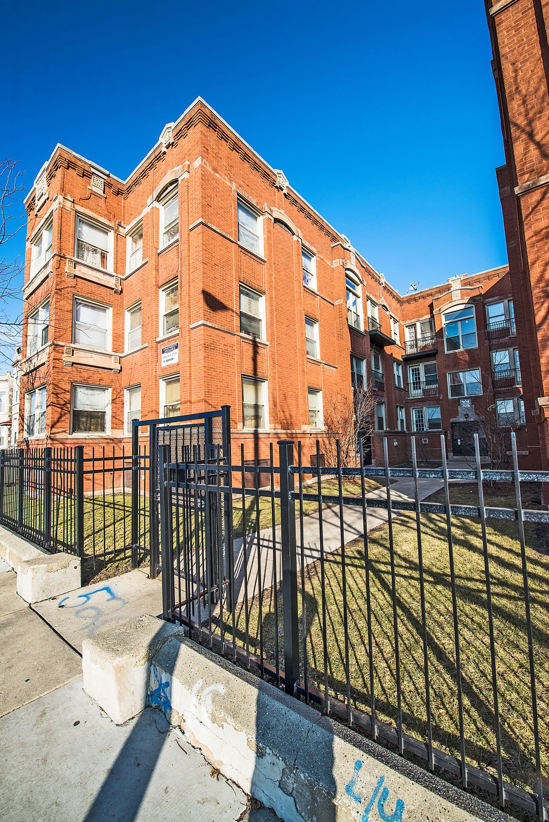 Brick apartment building with black fence, clear blue sky.