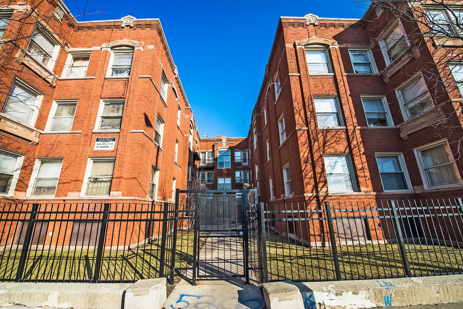 Brick apartment buildings with black fences and gate under a blue sky.