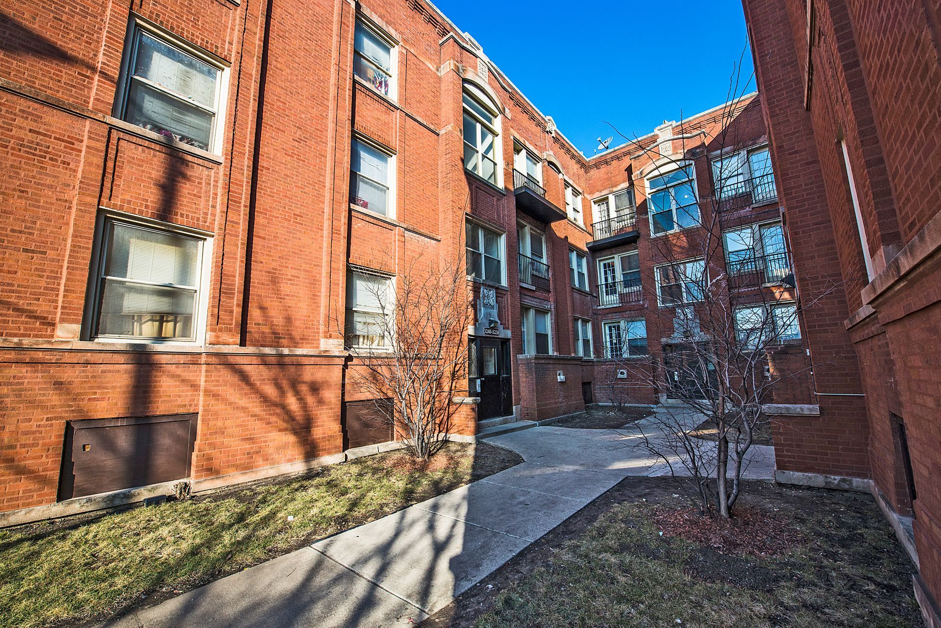 Red brick apartment building with courtyard, sunny day.