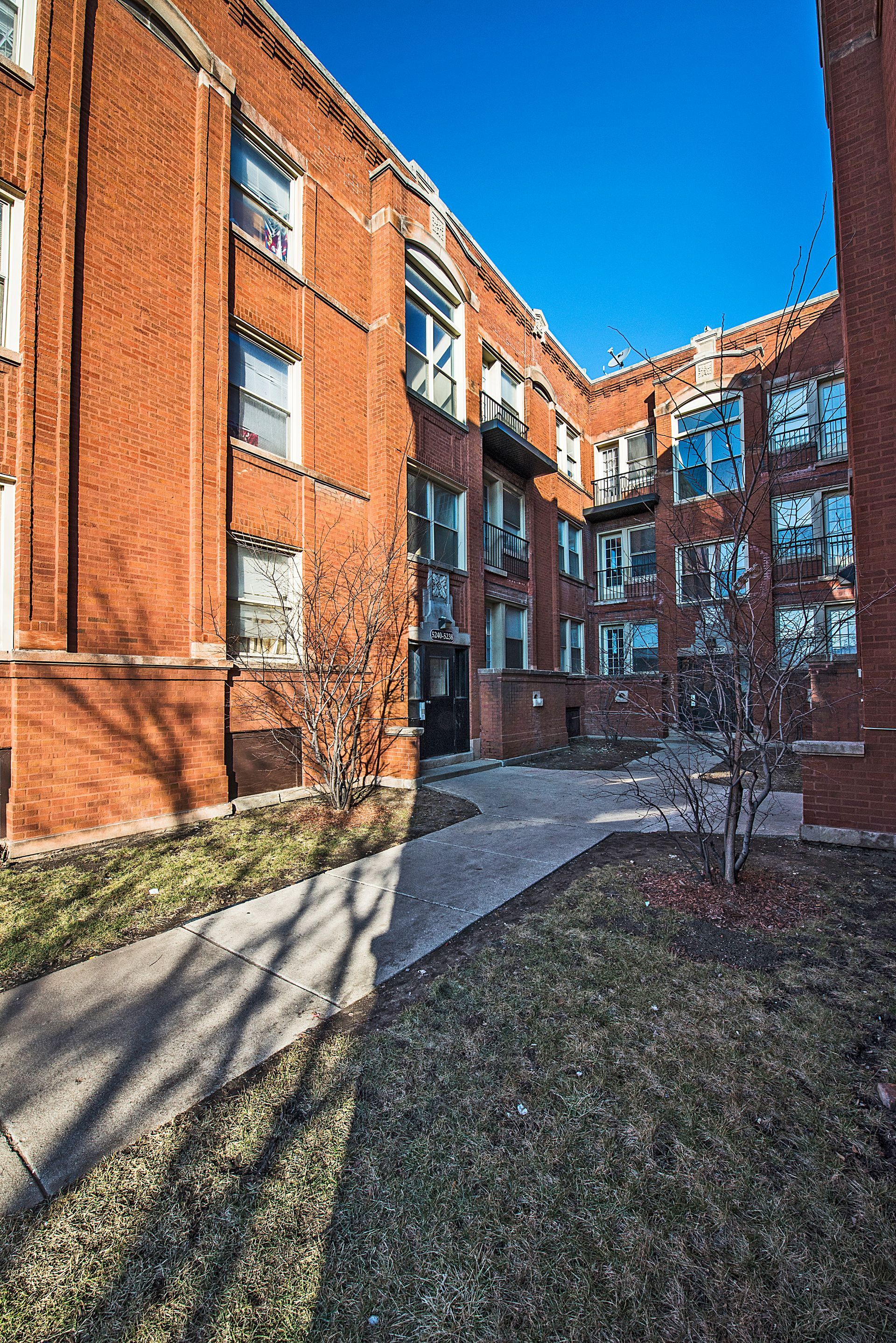 Red brick apartment building with courtyard, sunny day.