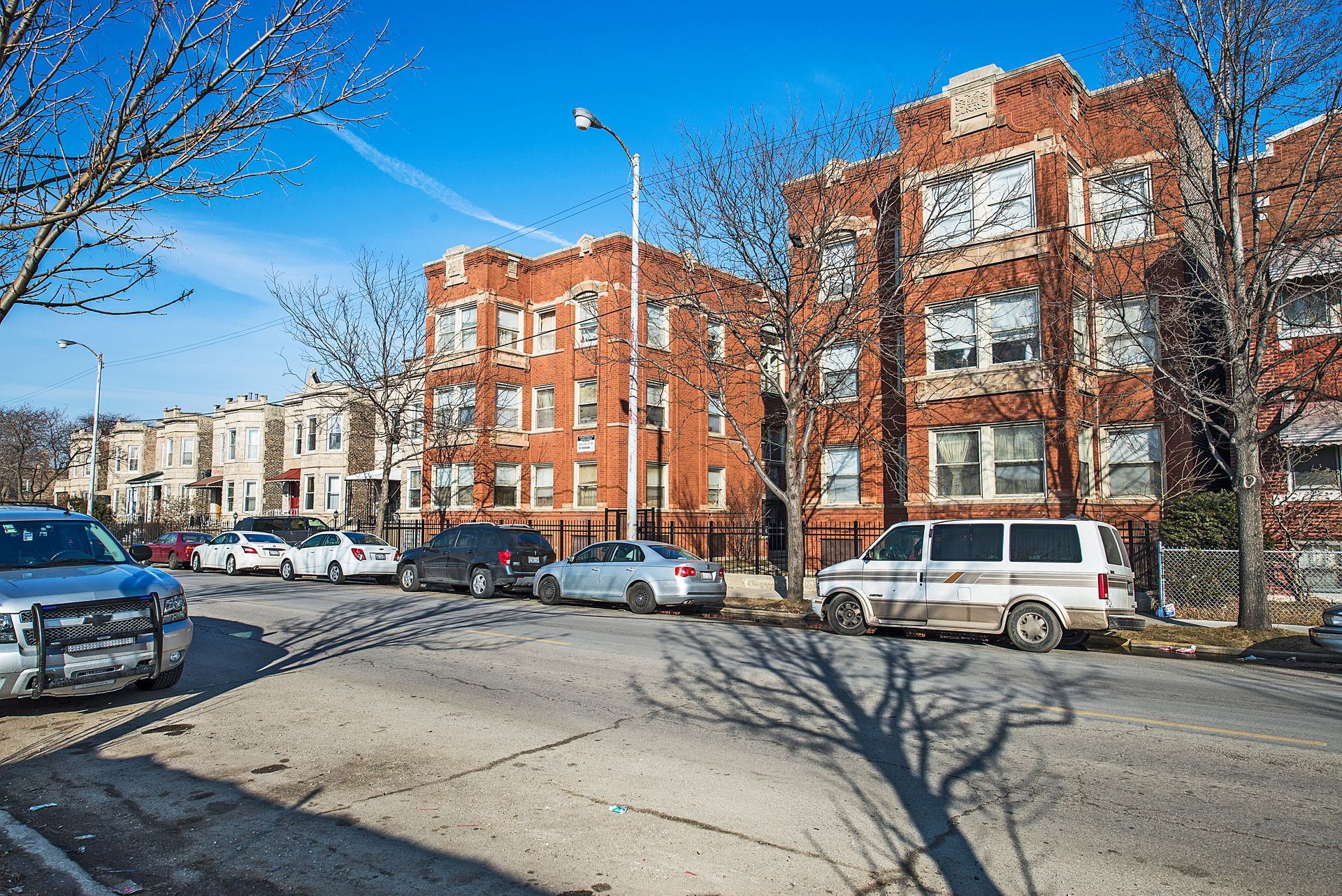 Street scene with brick apartment buildings and parked cars on a sunny day.