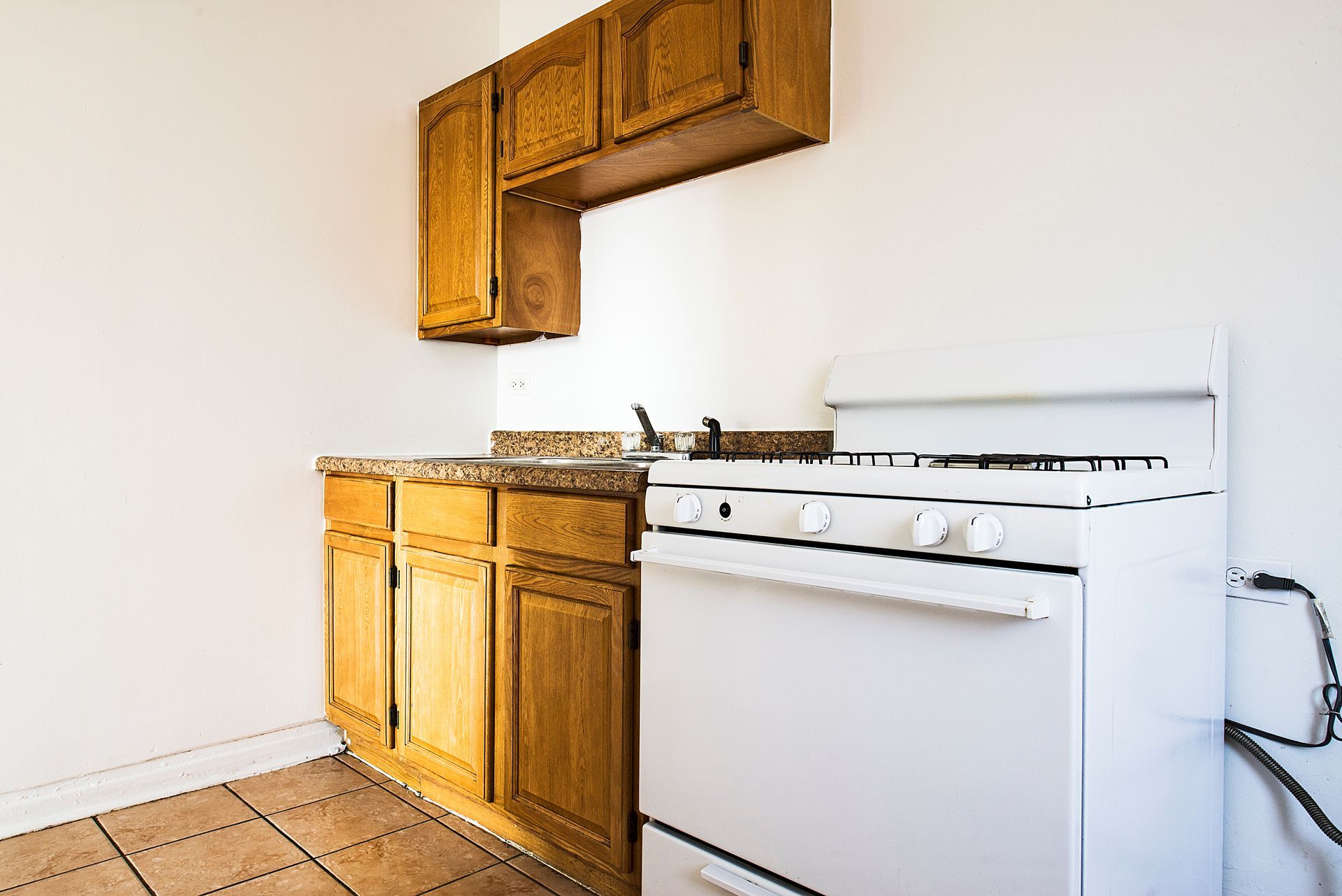 Small kitchen with white stove, wood cabinets, and tan countertops.