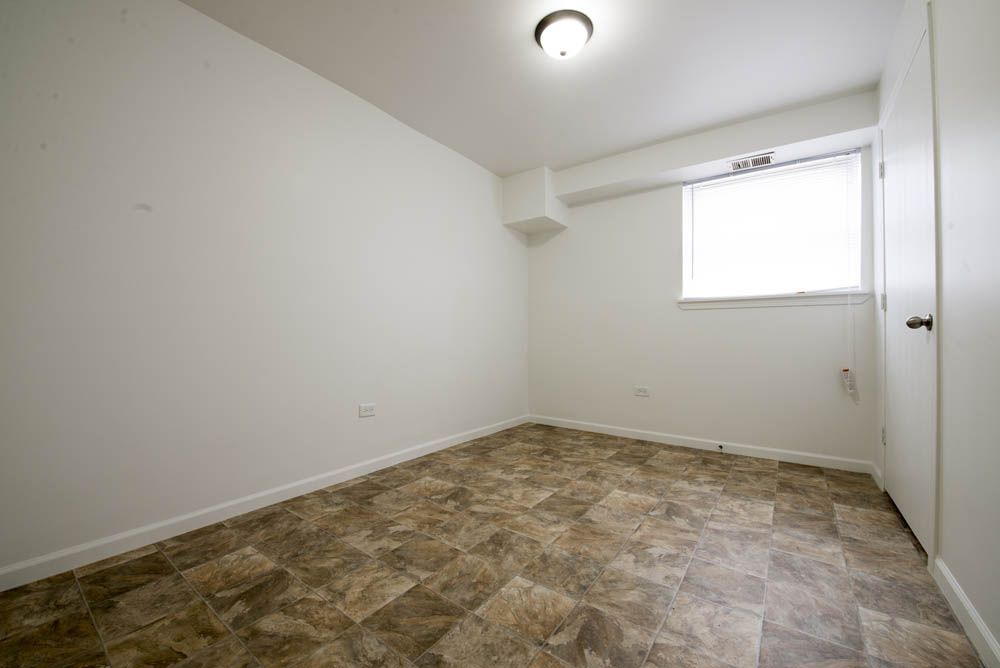 Empty room with tiled floor, white walls, small window, closed door, and ceiling light.