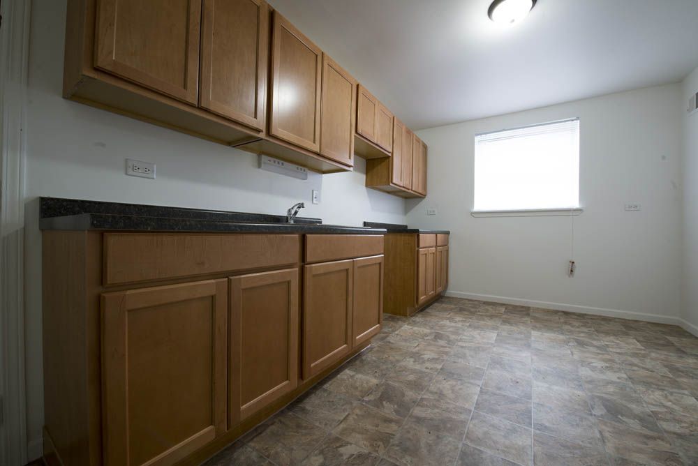 Empty kitchen with light brown cabinets, dark countertop, and linoleum flooring.