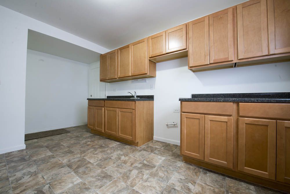 Empty kitchen with light wood cabinets, dark countertops, and linoleum floor.
