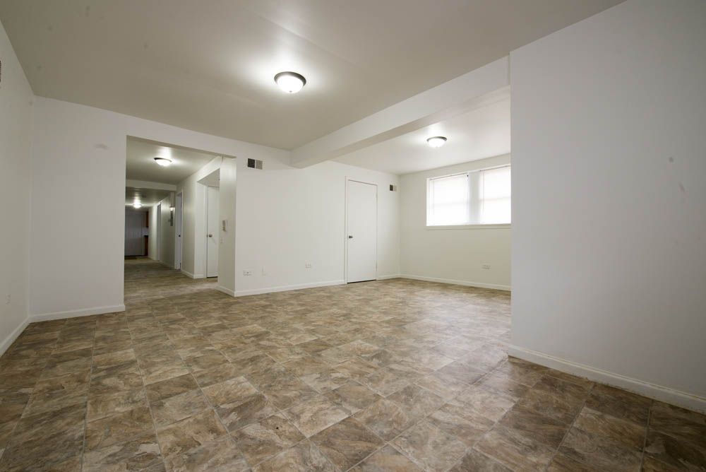 Empty room with brown and beige patterned flooring, white walls, and bright overhead lights.