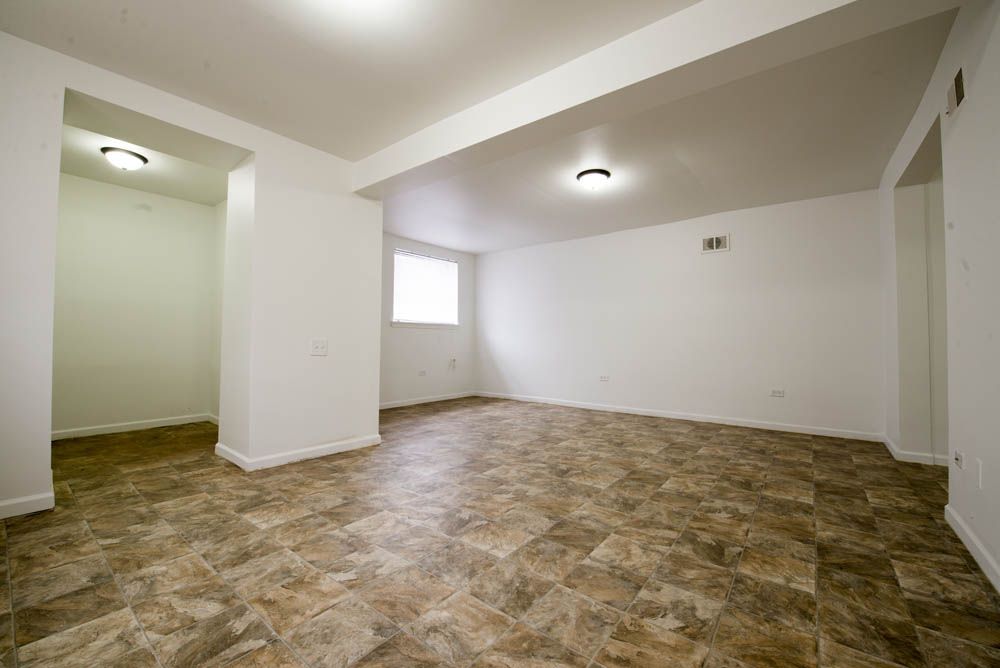 Empty room with brown and tan tiled floor, white walls, and a small window.