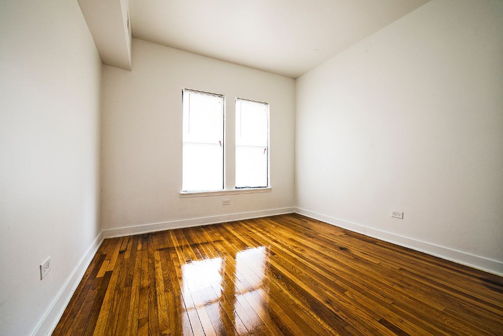 Empty room with hardwood floors, two windows, and white walls.