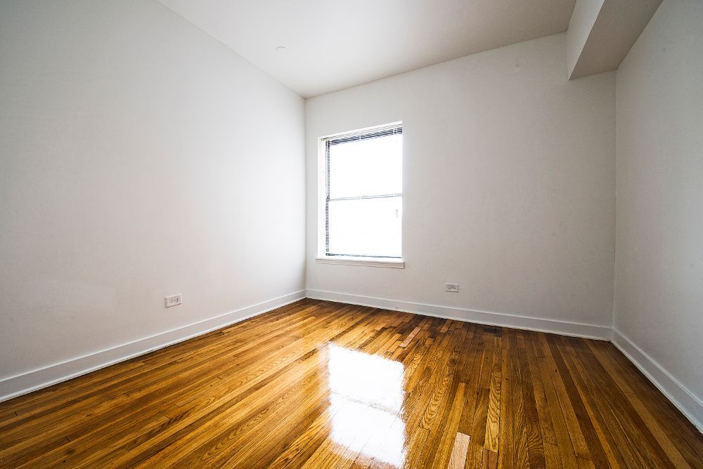 Empty room with hardwood floors, white walls, and a window.