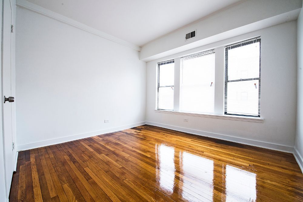 Empty room with wood floors and three windows with white walls.