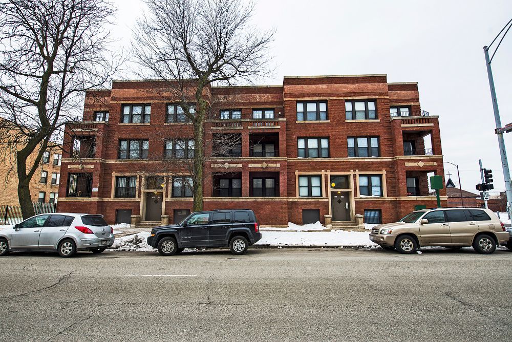 Red brick apartment building with cars parked out front, snow on the ground.