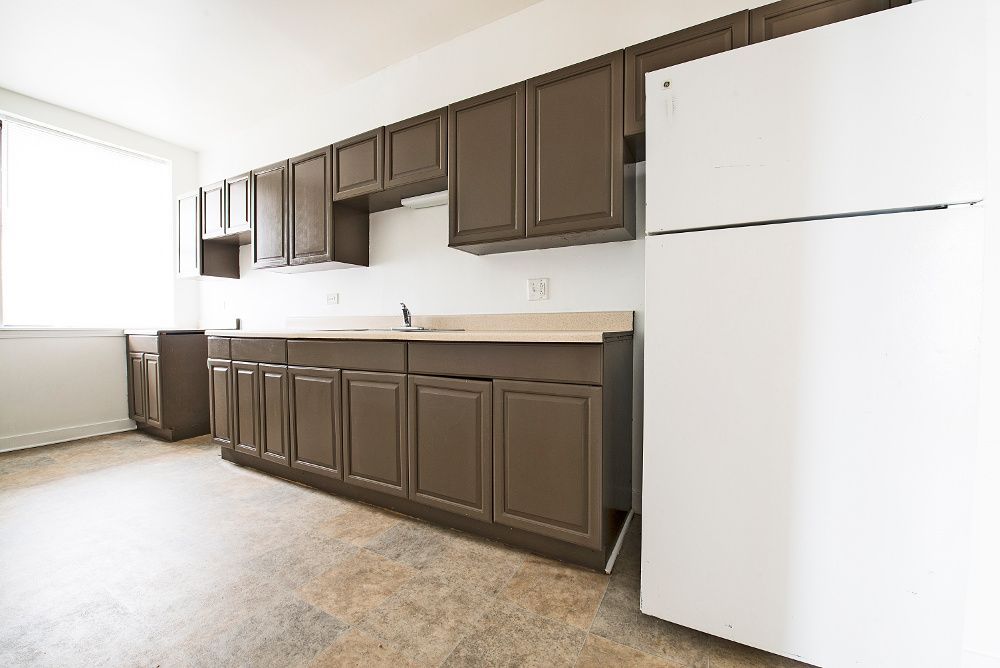 Brown kitchen cabinets, white appliances, and a window in a bright room.