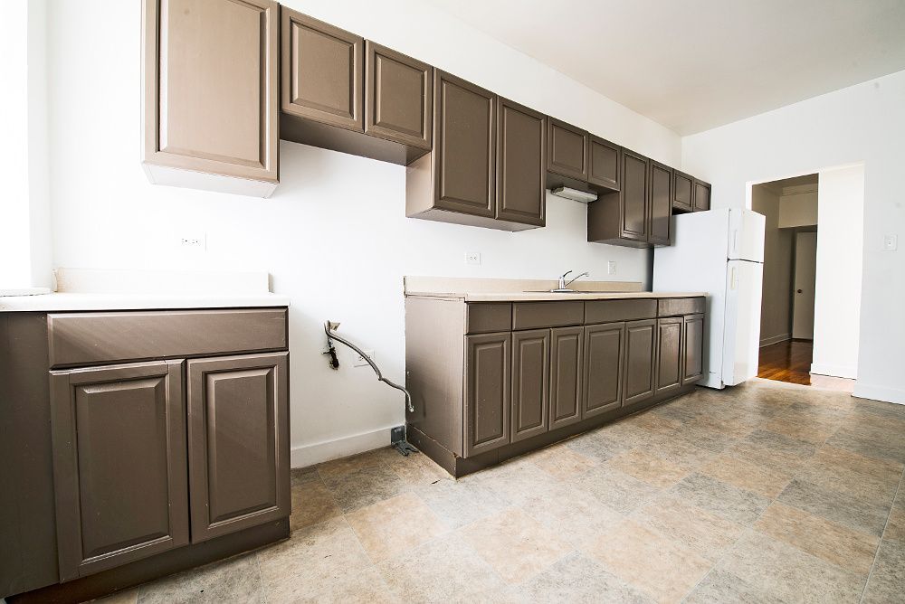 Empty kitchen with brown cabinets, white walls, and beige countertop.