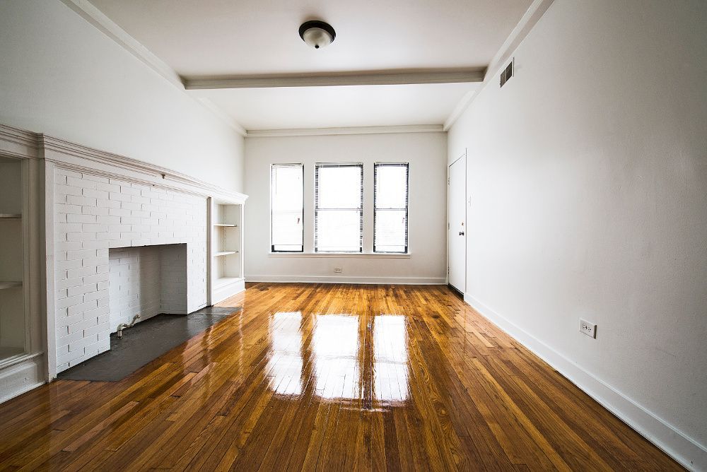 Empty room with hardwood floors, a fireplace, and windows reflecting sunlight.