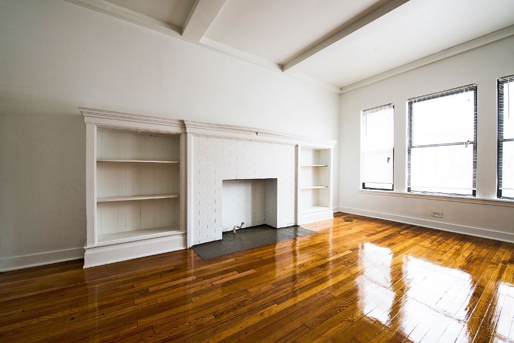 Empty living room with wood floor, white walls, built-in bookshelves, and fireplace.
