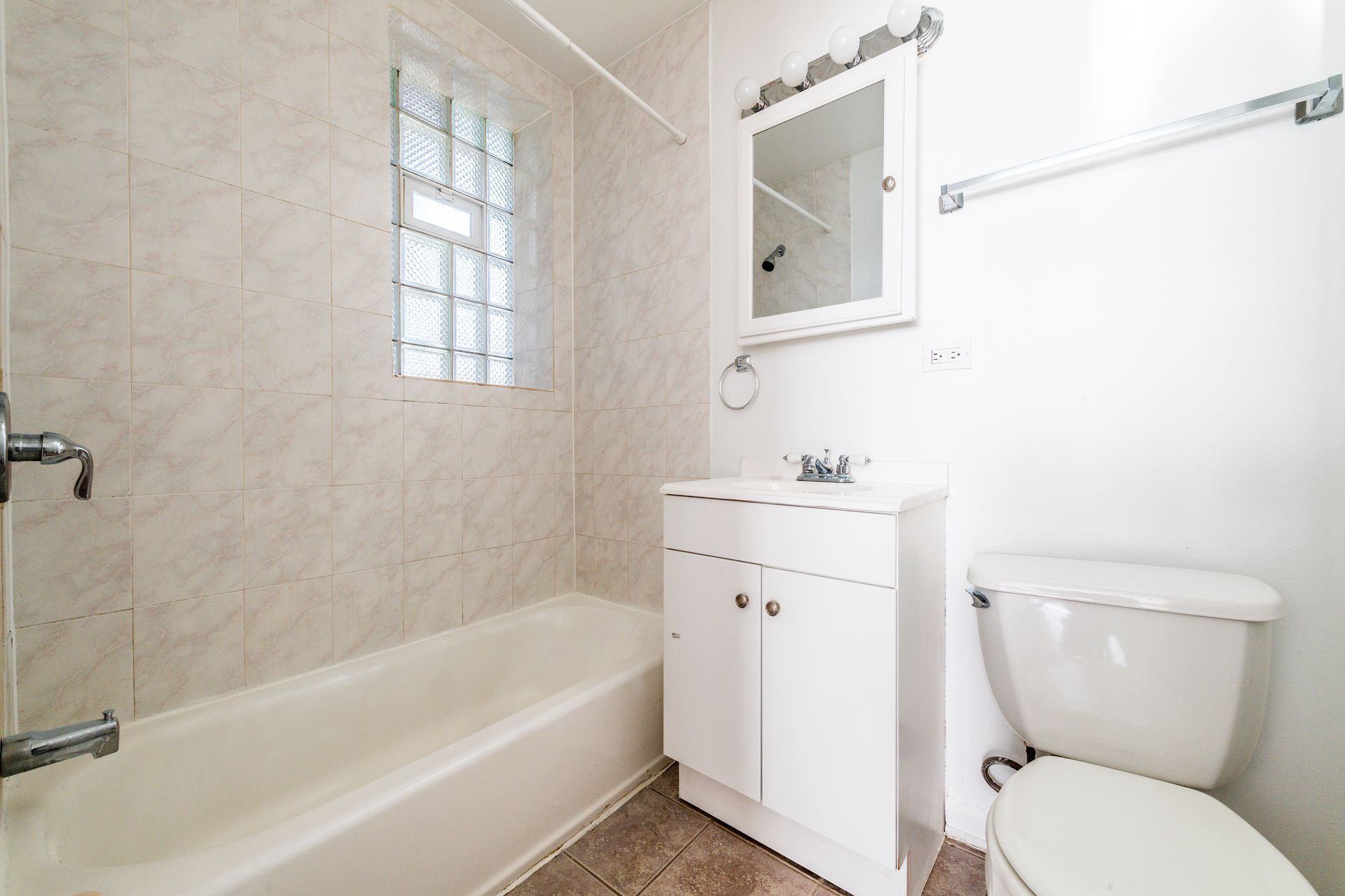 Bathroom with bathtub, toilet, vanity, and glass block window. White and neutral tones.