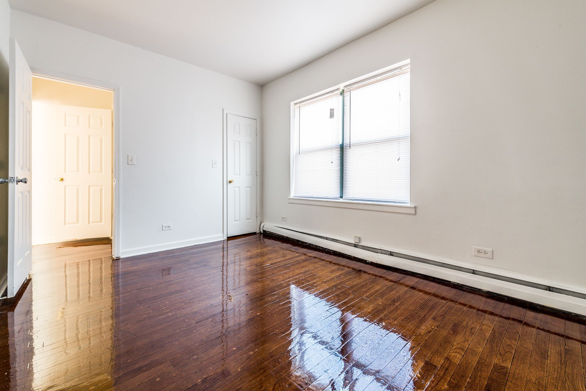 Empty room with dark wood floors, white walls, and a window.